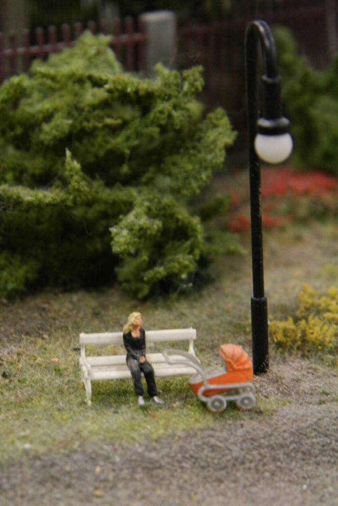 A mum takes a break on a park bench with her pram at Loxx Miniatur Welten Berlin