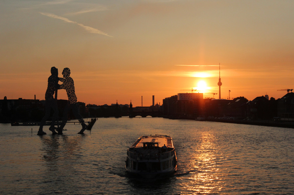 Sunset from Elsenbrücke Berlin with a view of the Molecule Man, Oberbaumbrücke and Fernsehturm and a boat on the River Spree