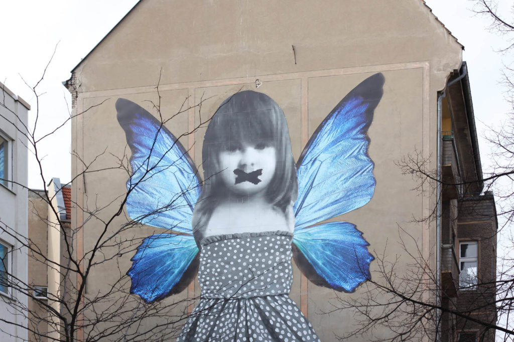 Butterfly Mural - Street Art by Michelle Tombolini in Berlin seen through the trees on Boxhagener Strasse in Friedrichshain