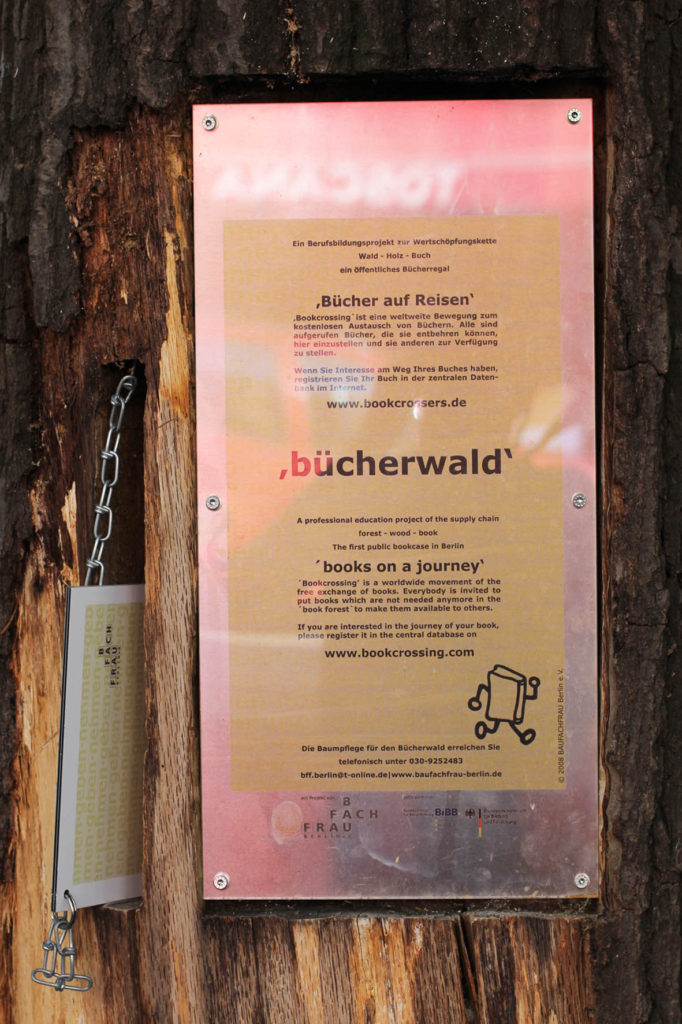 A plaque on the Bücherwald (book forest) - a lending library with shelves carved into logs bolted together to resemble a tree on Sredzkistrasse in Berlin Prenzlauer Berg. A professional education project of the supply chain forest – wood – book The first public bookcase in Berlin