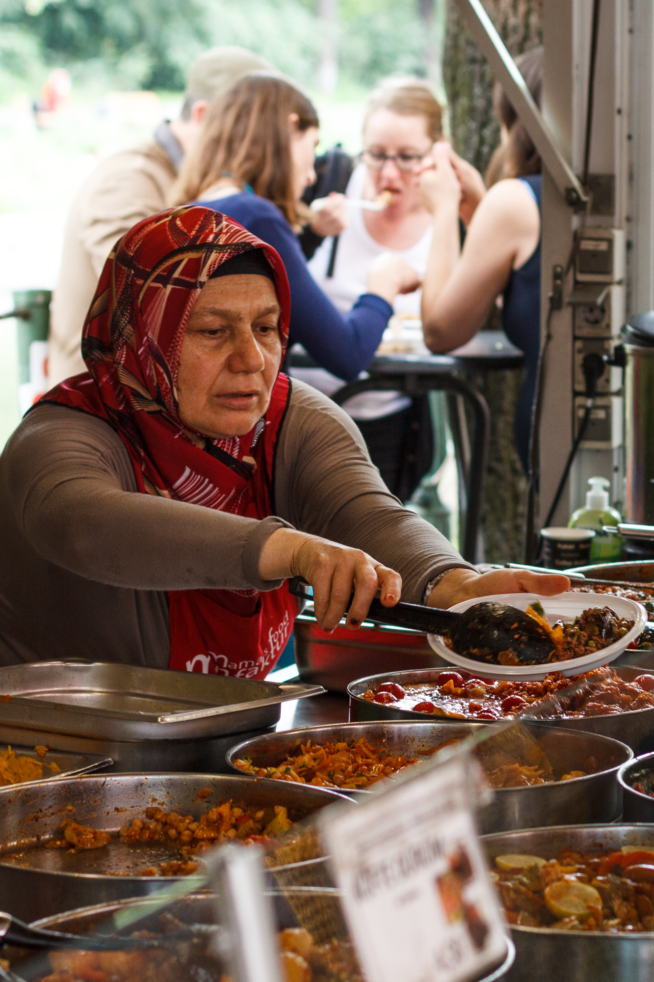 Eine Frau serviert Essen an dem Mamas Food Manufaktur Stand auf dem sehr bunten türkischen Markt am Maybachufer in Berlin Neukölln